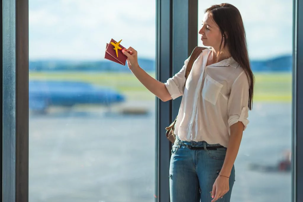 Frau mit Reisepass und Miniaturflugzeug in der Hand am Flughafen.
