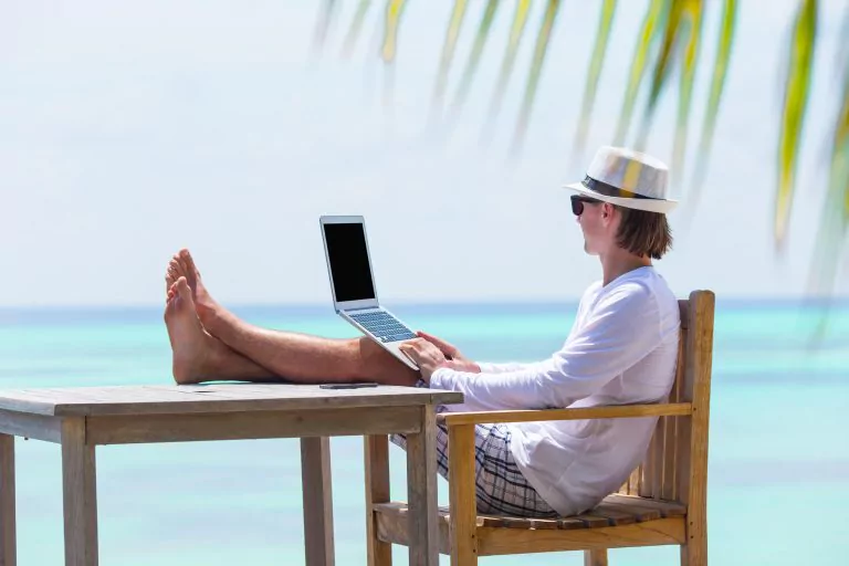 Frau mit Hut sitzt vor Laptop mit Blick auf das Meer