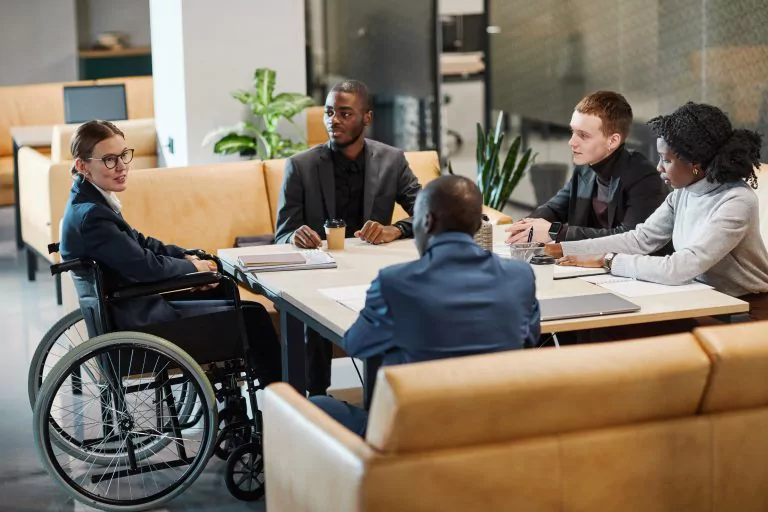 Rollstuhlfahrer sitzt mit anderen Kollegen rund um einen Tisch