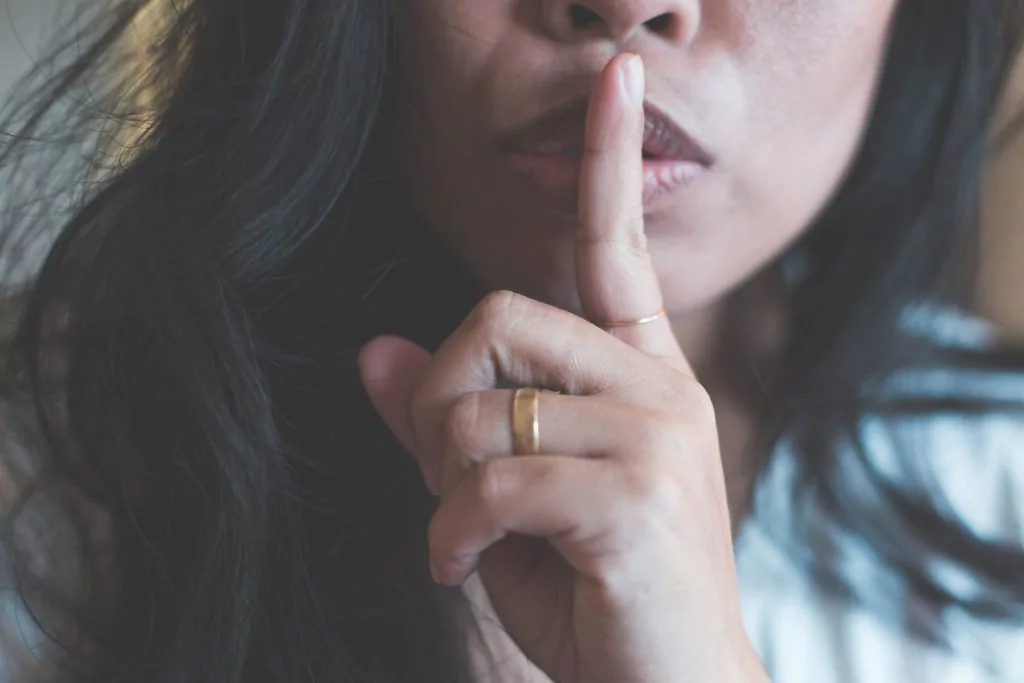 Frau hält sich den Finger vor den Mund als Zeichen von "Sei leise".