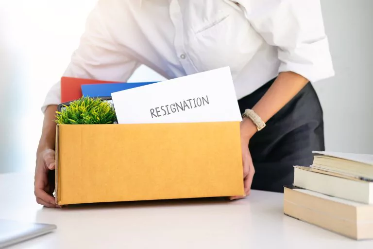 Mann hält Box in der Hand, die verschiedene Utensilien und ein Kuvert mit der Aufschrift "RESIGNATION" enthält