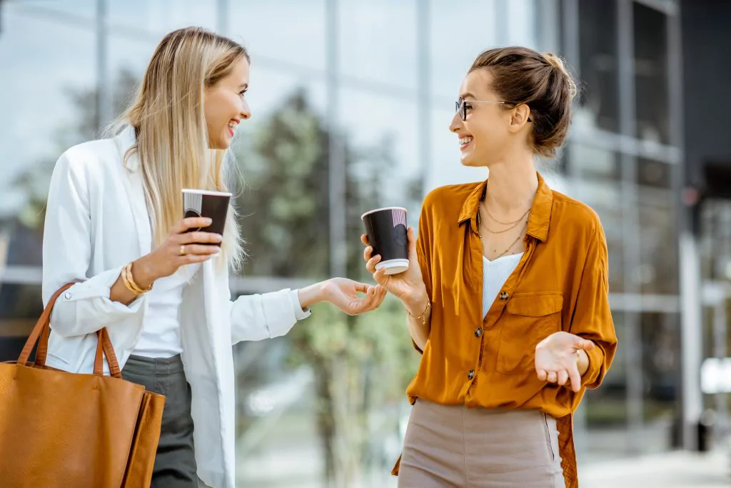 Zwei Frauen unterhalten sich lächelnd und trinken Kaffee. 