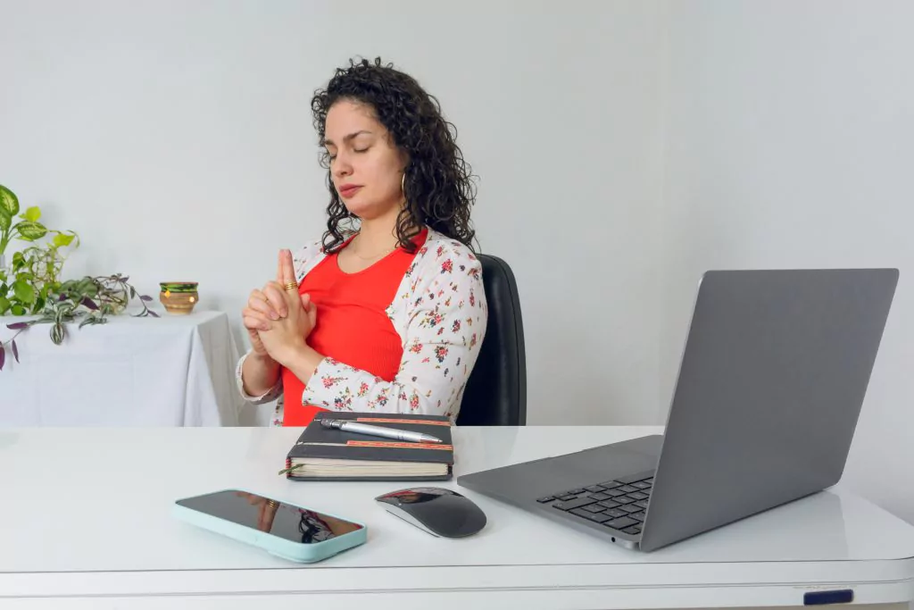 Frau sitzt am Schreibtisch vor Laptop und macht Entspannungsübungen