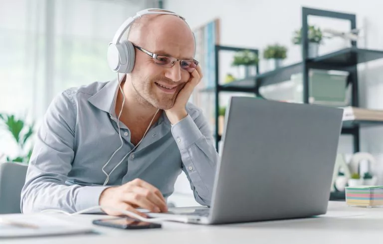 Mann sitzt mit Kopfhörern vor einem PC und lächelt