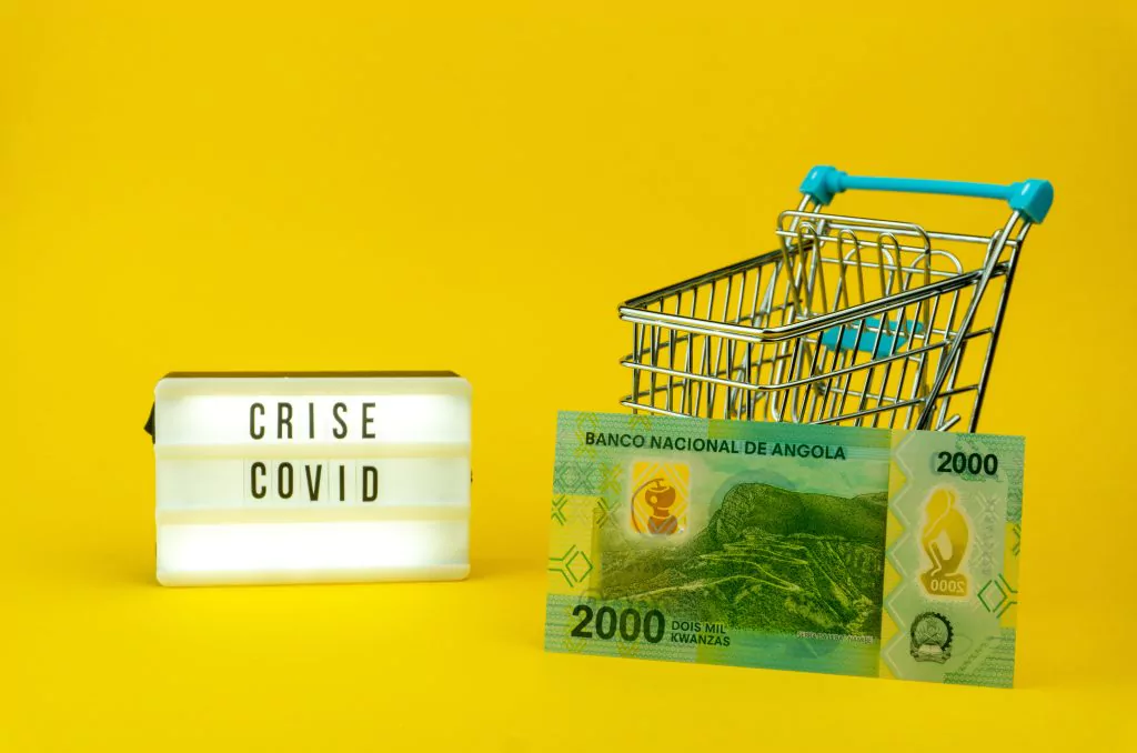 Gelber Hintergrund mit einem Schild auf dem Crisis Covid steht sowie ein Einkaufskorb und davor eine Banknote mit 2000
