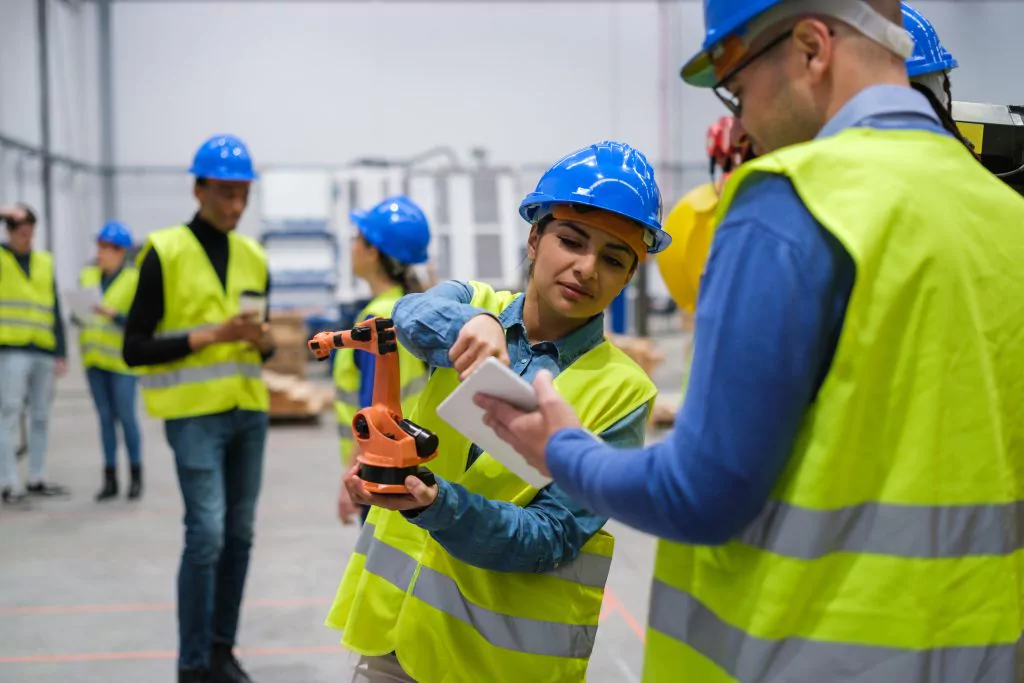 Mann und Frau mit gelben Sicherheitswesen und blauen Helmen halten einen orangen Roboter in ihren Händen